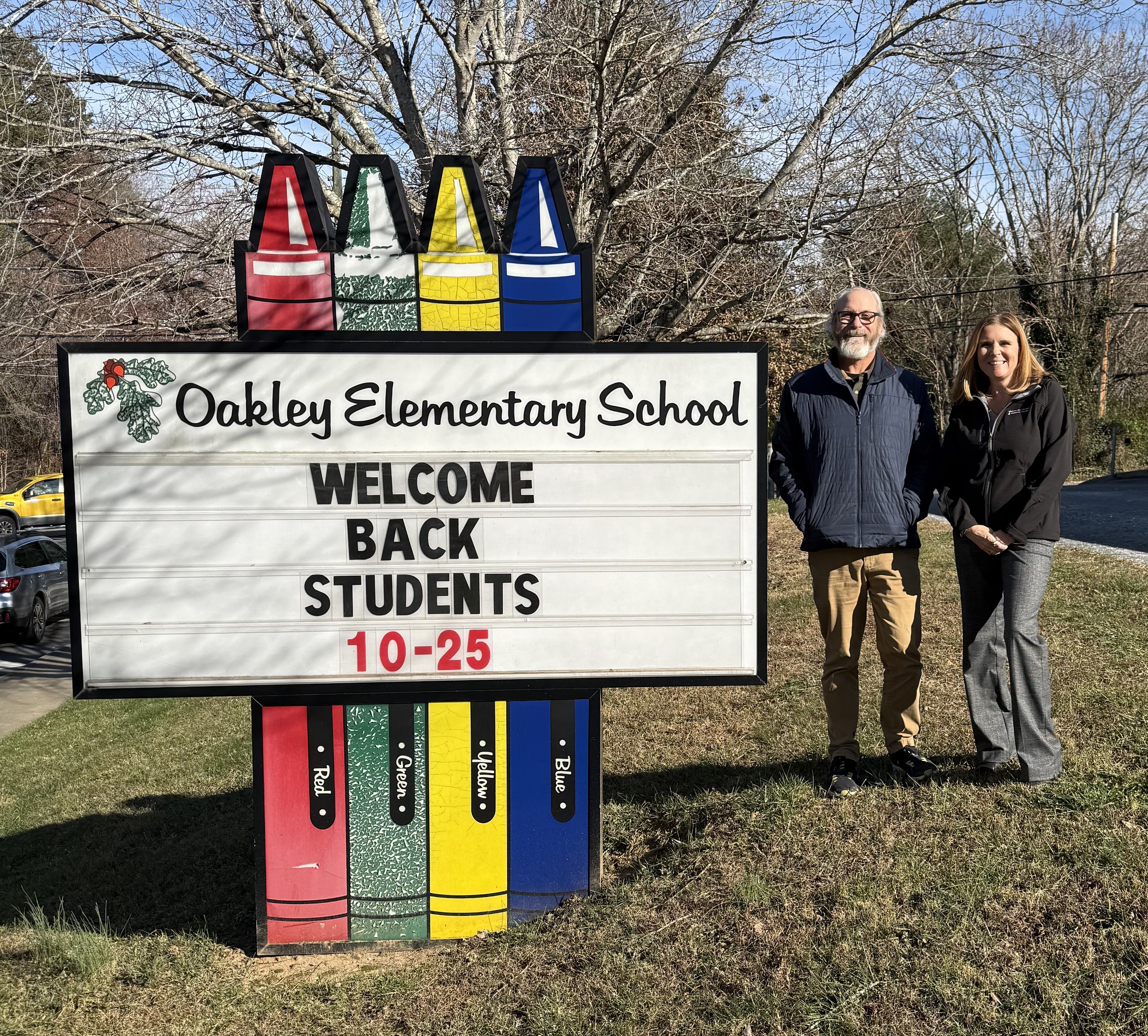 Jim Hand & Kim Creamer stand beside the Oakley Elementary School sign